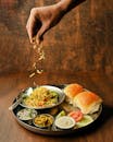 A close-up of misal pav, a spicy Indian dish, with toppings being added by hand.