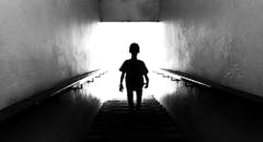 A dramatic black and white silhouette of a child climbing stairs towards light, symbolizing hope and discovery.